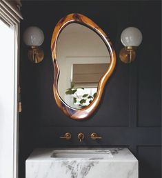 a marble sink and mirror in a room with black walls, gold fixtures and lights