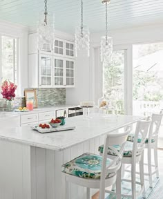 a large kitchen with white cabinets and marble counter tops, along with two bar stools