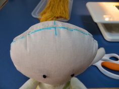 a white stuffed animal sitting on top of a blue table next to scissors and yarn