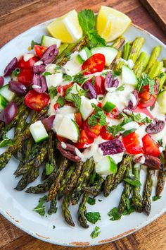 a white plate topped with asparagus, tomatoes and other veggies on top of a wooden table