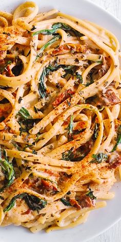 a white plate topped with pasta covered in sauce and spinach leafy toppings