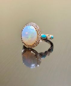 an opal and diamond ring on a reflective surface