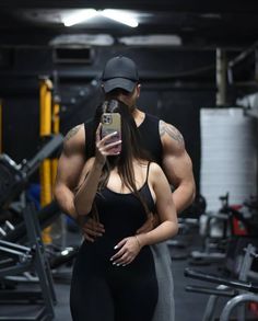 a woman taking a selfie with a man in the background wearing a black cap and leggings