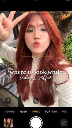 a girl with long red hair is making a hand gesture to the camera while wearing a white shirt