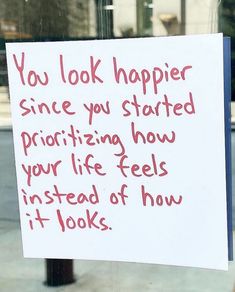 a sign posted on a pole in front of a store window that says, you look happier since you started praizing how your life feels instead of how it looks