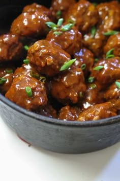 meatballs with sauce in a black bowl on a white counter top, ready to be eaten