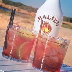 two glasses filled with drinks sitting on top of a table next to an empty bottle