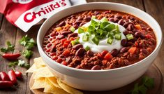 a white bowl filled with chili and sour cream on top of tortilla chips