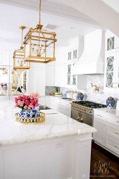 a white kitchen with marble counter tops and gold accents on the hood, oven, sink, and stovetop