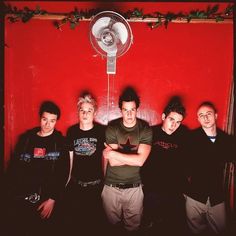 a group of young men standing next to each other in front of a red wall