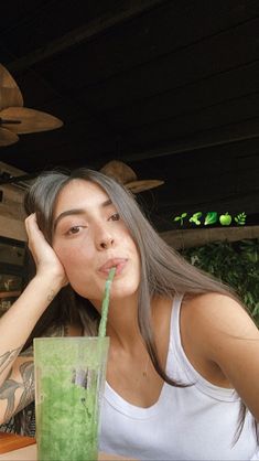 a woman sitting at a table with a green drink in front of her and another person behind her