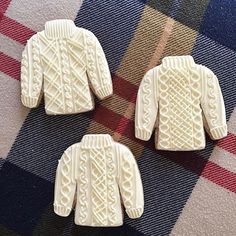 three white knitted sweaters sitting on top of a checkered table cloth next to each other