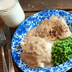 a blue and white plate topped with mashed potatoes, peas and gravy