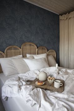 an unmade bed with white linens and two cups of coffee on the tray