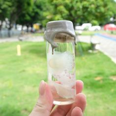 a person holding up a glass filled with ice and water in front of a park