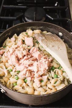 a skillet filled with pasta and meat on top of a stove next to a wooden spoon