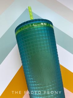 a green glass sitting on top of a yellow and white tablecloth next to a cup with a straw in it