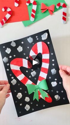 two hands are holding up a card with candy canes on it and paper decorations