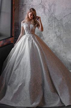 a woman in a silver and gold wedding dress standing next to a brick wall with her hand on her head