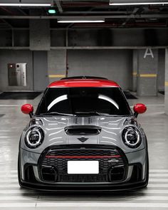 the front end of a grey mini cooper in a parking garage with red lights on