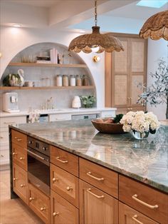 a large kitchen with wooden cabinets and marble counter tops, along with a bowl of flowers on the island