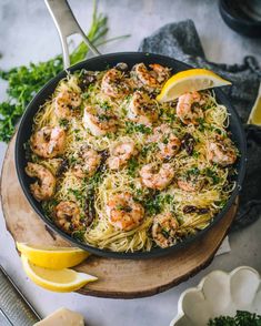 shrimp and pasta in a skillet with lemon wedges next to it on a cutting board