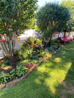 a garden with lots of plants and flowers in it's bed next to a white picket fence