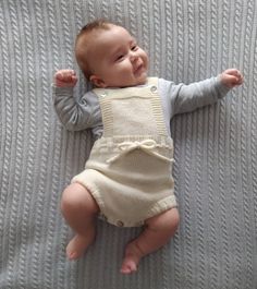 a baby laying on top of a bed next to a gray blanket and smiling at the camera