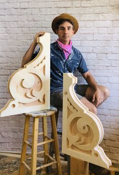 a man sitting on top of a stool next to a wooden chair that has been carved into it