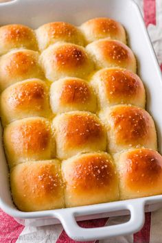 a white casserole dish filled with bread rolls on a red and white tablecloth