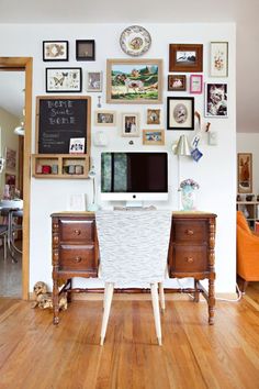 a desk with a computer on top of it in front of a wall full of pictures