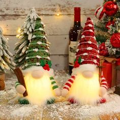 two christmas gnomes sitting in the snow next to small trees and bottles of wine