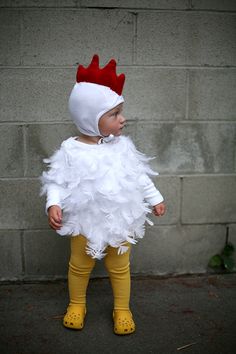 a toddler in a chicken costume standing next to a brick wall