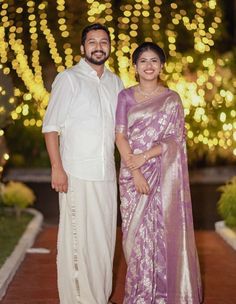 a man and woman standing next to each other in front of a tree with lights