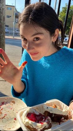 a woman sitting at a table with plates of food in front of her and one hand up to the camera