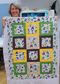 a woman holding up a quilt made to look like it has many animals on it