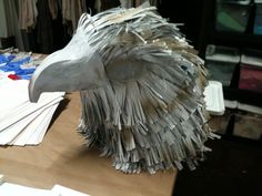 an eagle sculpture made out of newspaper strips on a wooden table next to other papers