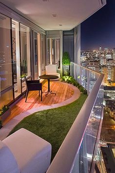 a balcony overlooking the city at night with chairs and table on grass covered flooring