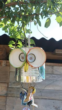 an owl made out of tin cans is hanging from a tree branch with other items attached to it