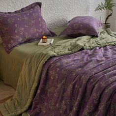 a bed with purple and green comforters on top of it next to a potted plant