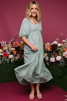 a woman standing in front of flowers wearing a green dress