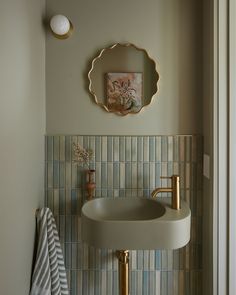 a bathroom sink sitting under a mirror next to a wall mounted faucet with a painting on it