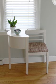 a small white table with a plant on it next to a window in a room