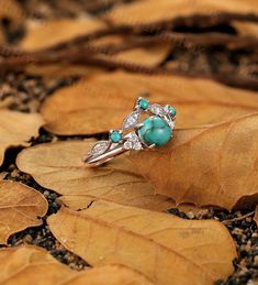 a ring with turquoise stones and diamonds on top of leafy brown leaves in the woods