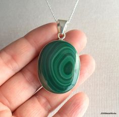 This gorgeous oval bullseye malachite pendant is suspended on a 24 inch sterling silver 1mm cable chain. It is perfect for any occasion! Pendant height: 1.9 inches or 50mm, including bail Pendant width, at widest point: 1.1 inches or 28mm Pendant setting and bail: sterling silver You will receive the exact piece of jewelry pictured. Convo me for a different length chain (additional charges may apply). Metaphysical properties (not backed by science): Malachite is a protection stone, absorbing neg Oval Malachite Necklace As Gift, Oval Malachite Gemstone Jewelry, Green Oval Malachite Necklaces, Green Oval Malachite Necklace, Elegant Malachite Round Pendant Necklace, Malachite Pendant Necklace With Natural Stones, Elegant Malachite Pendant Jewelry, Artisan Malachite Pendant Necklace, Silver Malachite Pendant Necklace