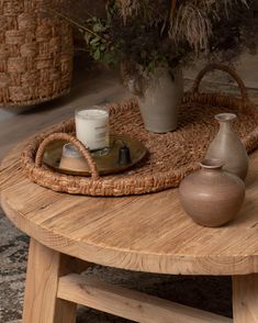 a wooden table with two vases and a candle on it, sitting next to a wicker basket