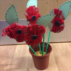 yarn wrapped flowers in a flower pot with green straws on the top and two red sticks sticking out of them