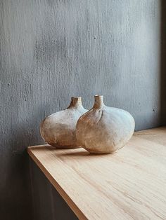 two white vases sitting on top of a wooden table next to a gray wall