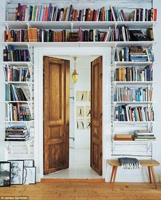 a bookshelf filled with lots of books next to two wooden doors in a room