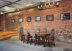 a brick wall with pictures on it and chairs around the table in front of it